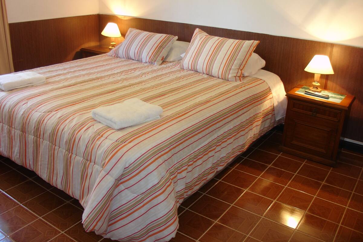 A hotel room with a large bed, two bedside tables, and two lamps.