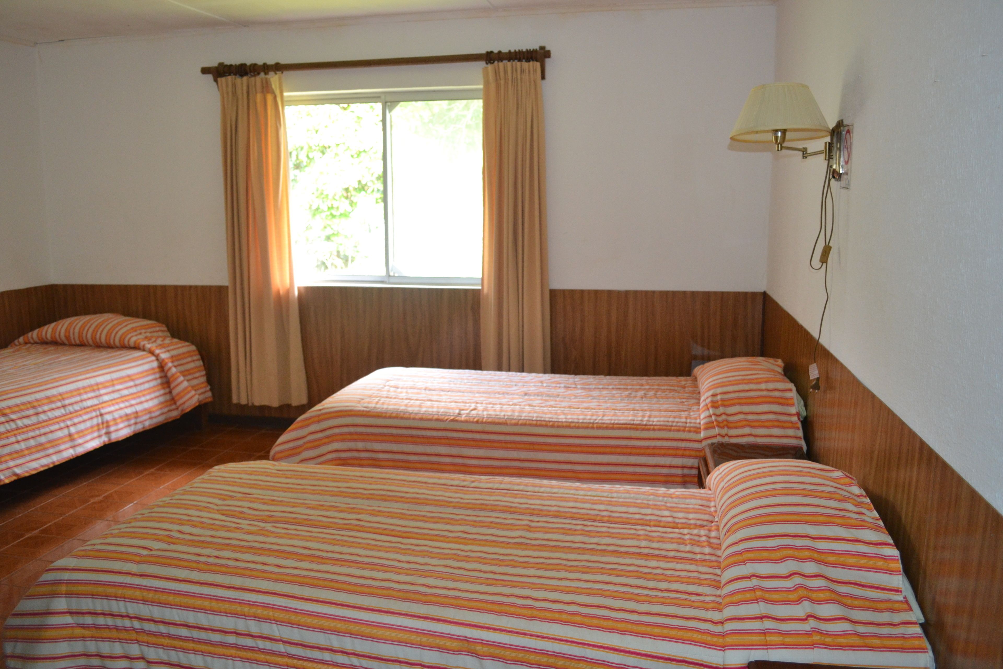 Una habitación con dos camas, una ventana con cortinas y una lámpara fijada a la pared.