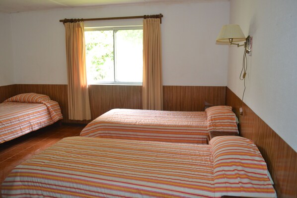 A room with two beds, a window with curtains, and a wall-mounted lamp.