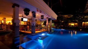 A poolside bar area with a pool illuminated by blue lights, surrounded by pillars and flags. - Bounty Hotel (Kuta)