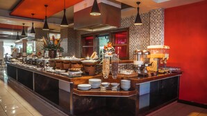 A buffet area with a variety of food items, including fruits, cereals, and beverages, arranged on a marble counter with overhead lighting. - Bounty Hotel (Kuta)