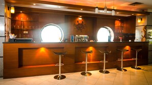 Een bar met een houten toonbank, barstoelen en een decoratieve stuurmanstoel.