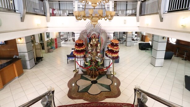 Een ruime lobby met een centraal decoratief kunstwerk, een kroonluchter en een receptiebalie.