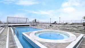 Een zwembad op het dak met een jacuzzi, ligbedden en uitzicht op de skyline van de stad.
