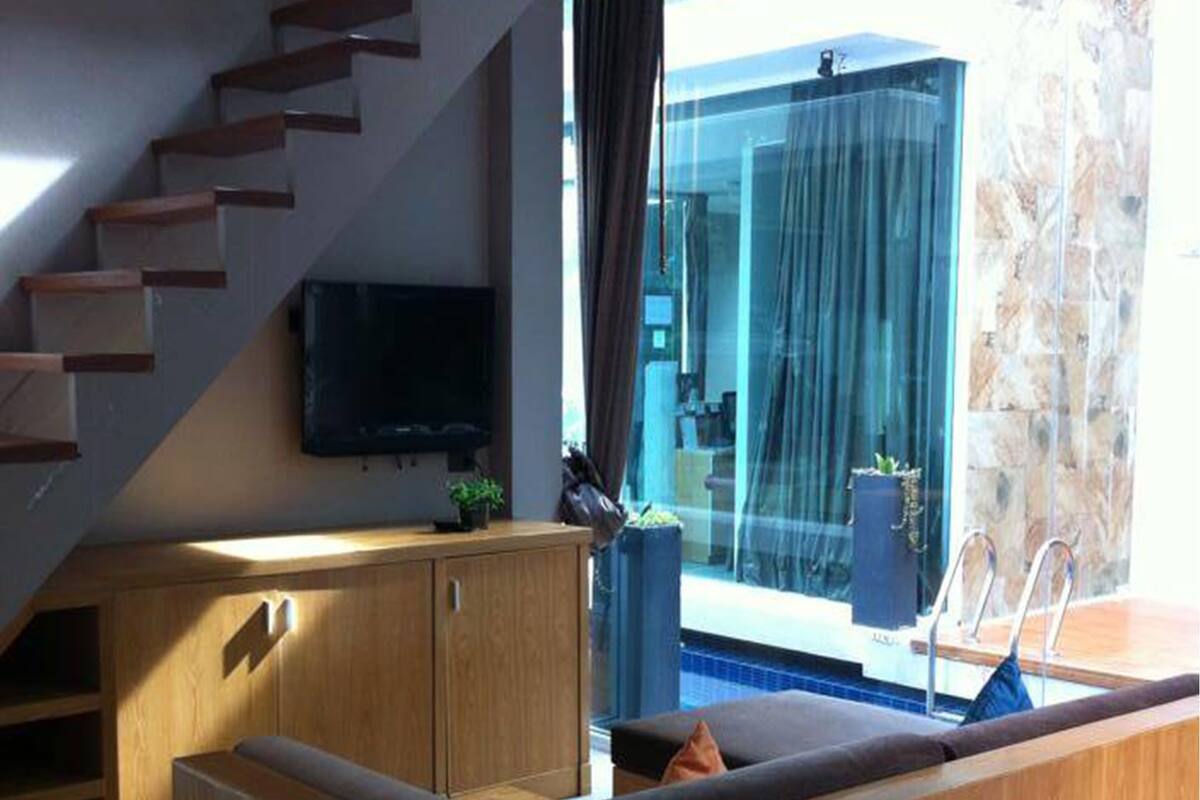 A modern living space with a wooden bench, a television, and a glass door leading to a pool area.