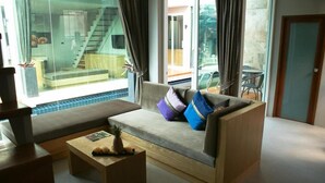 A modern living room with a sofa, a coffee table, and a glass wall offering a view of a staircase and outdoor seating. - P10 Samui (Koh Samui)