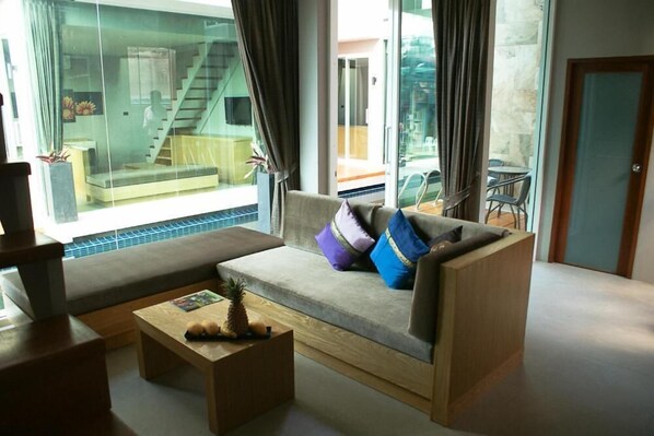 A modern living room with a sofa, a coffee table, and a glass wall offering a view of a staircase and outdoor seating. - P10 Samui (Koh Samui)