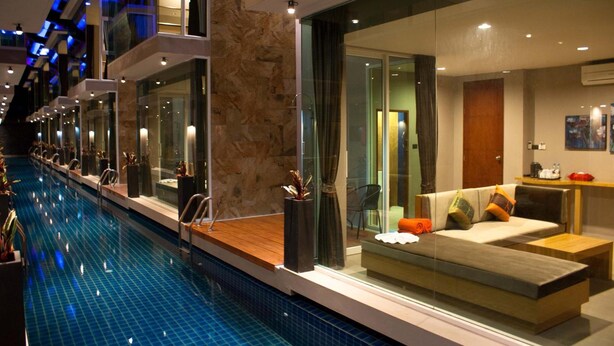 A modern hotel interior with a swimming pool, glass-enclosed seating area, and a stone accent wall. - P10 Samui (Koh Samui)