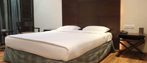 Ein Hotelzimmer mit einem großen Bett, einem Holzkopfstück, einem Nachttisch mit Lampe und einer Steckdose an der Wand.