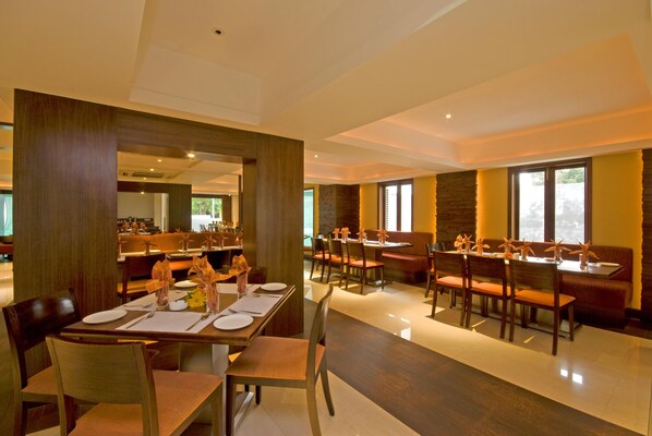 A spacious dining area with multiple tables and chairs, a central bar area, and large windows providing natural light. - Shantai Hotel (Pune)