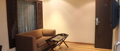 A small, furnished room with a sofa, a small table, and a door with a number.