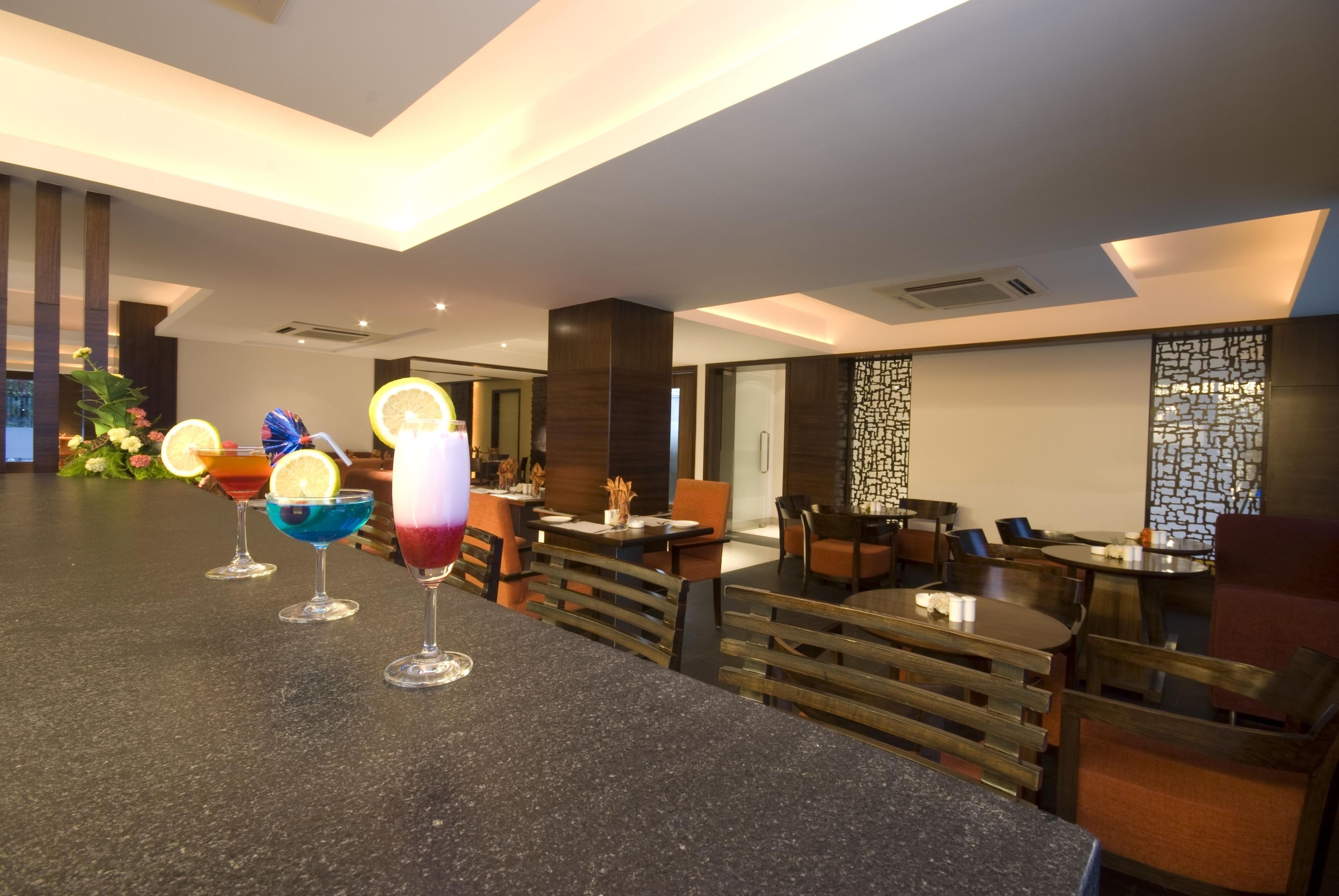 Eine moderne Bar mit einer Granitabdeckung, mehreren farbenfrohen Cocktails und einer Sitzecke mit Holztischen und -stühlen.