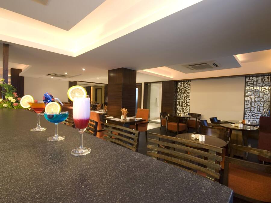 Eine moderne Bar mit einer Granitabdeckung, mehreren farbenfrohen Cocktails und einer Sitzecke mit Holztischen und -stühlen.