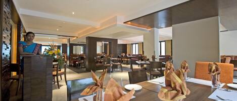 A modern dining area with a high ceiling, a reception desk, and a view of the dining space.