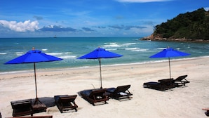 Una playa con tres sombrillas azules y sillas de descanso.
