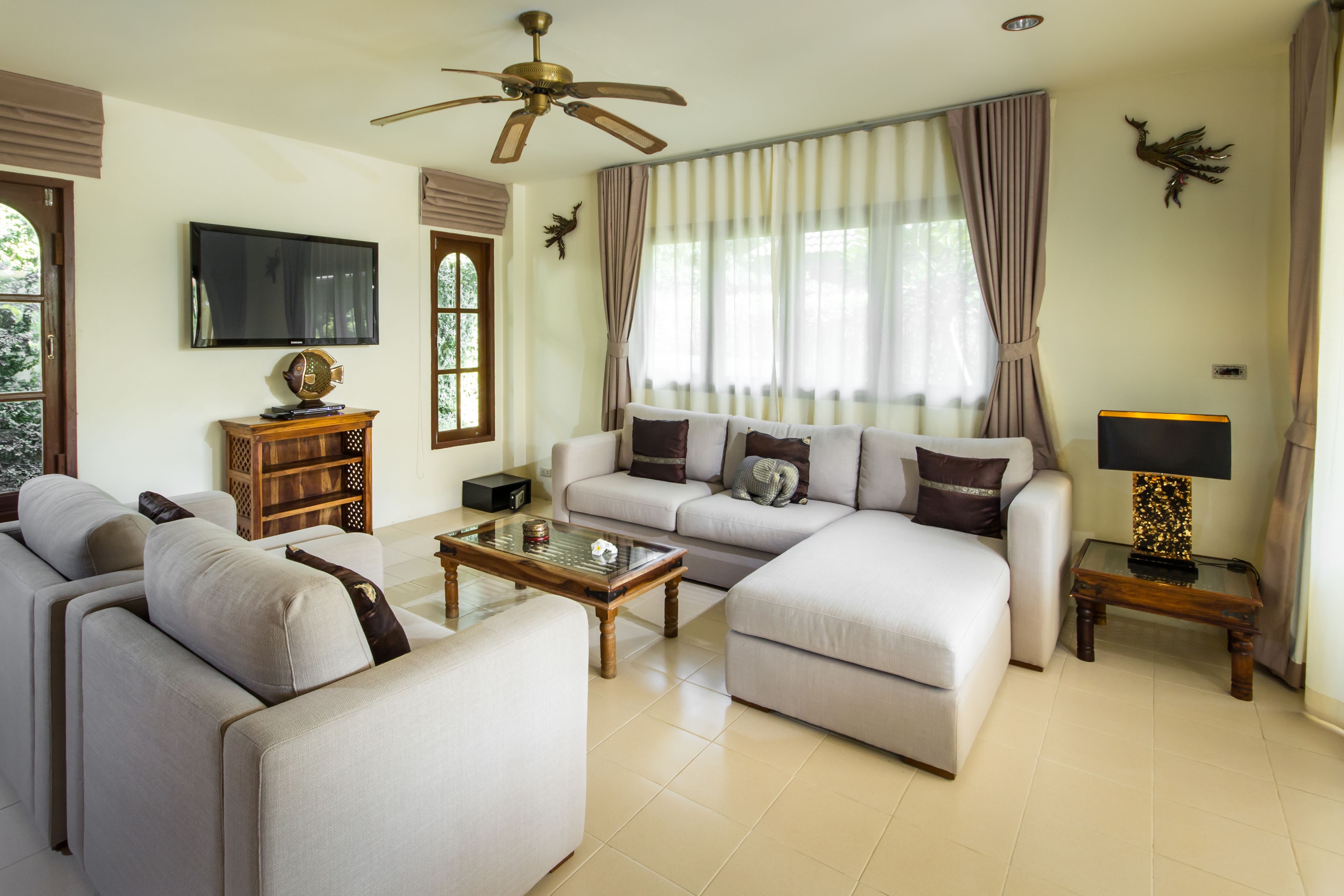A spacious living room with a ceiling fan, a flat-screen TV, a wooden coffee table, and a sofa set.