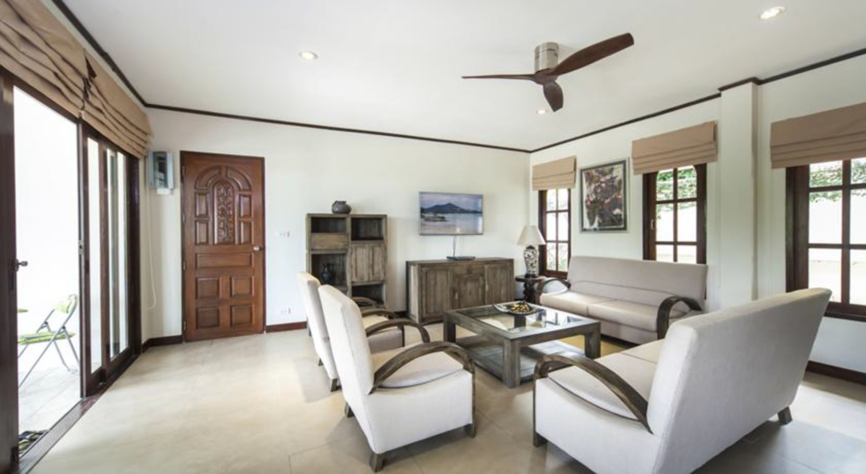 A spacious living room with a high ceiling, a ceiling fan, a large window with a view, and a door with a decorative design.