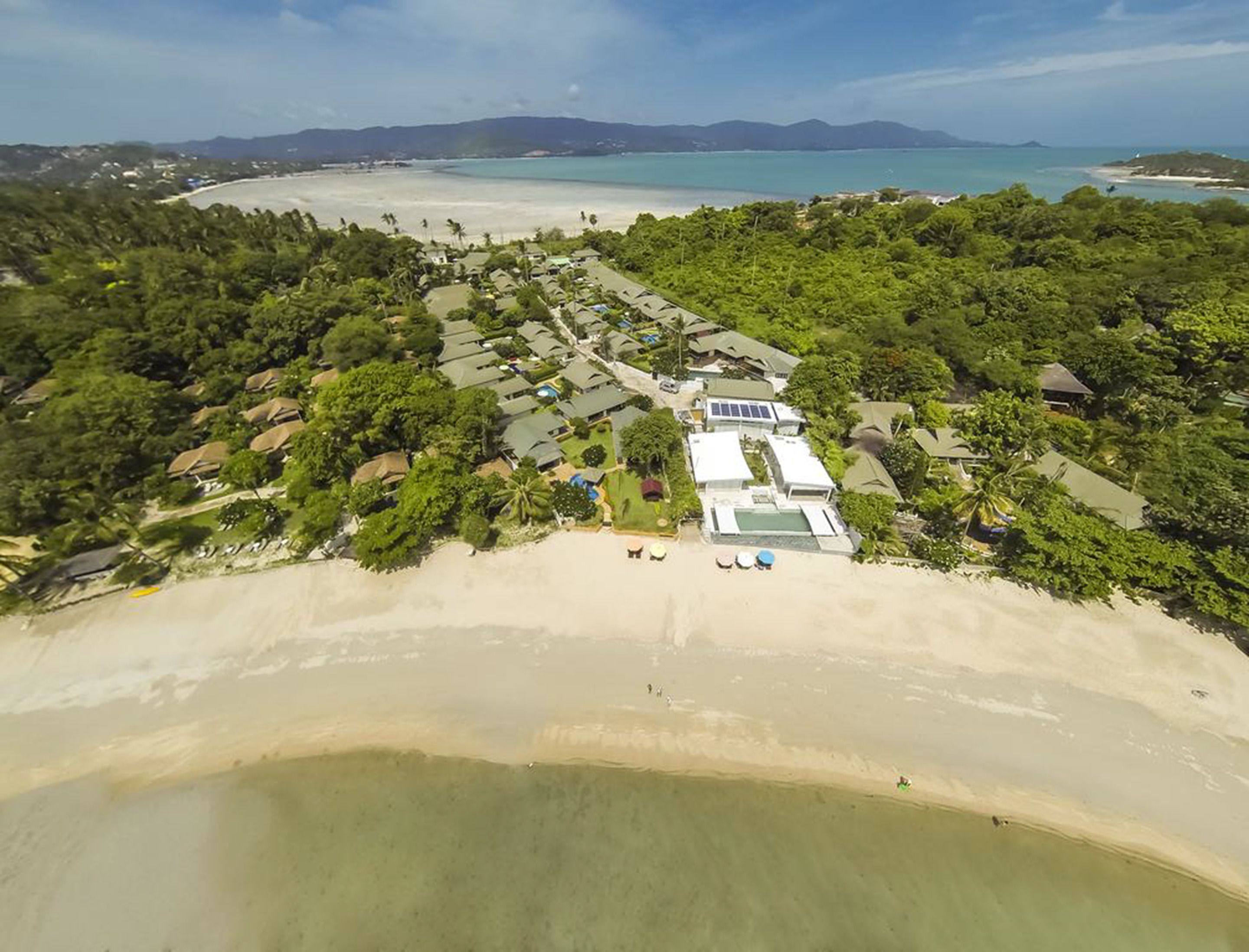 Oversigtsbillede af et resort med flere huse i bungalowstil, en strand og frit udsyn til havet.