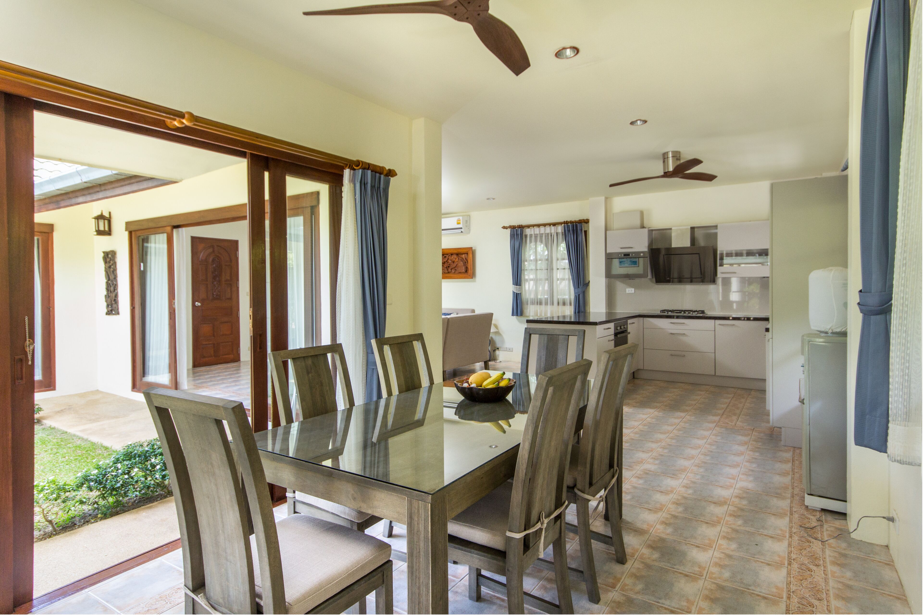 A dining area with a glass table and chairs, a kitchen with modern appliances, and a ceiling fan.