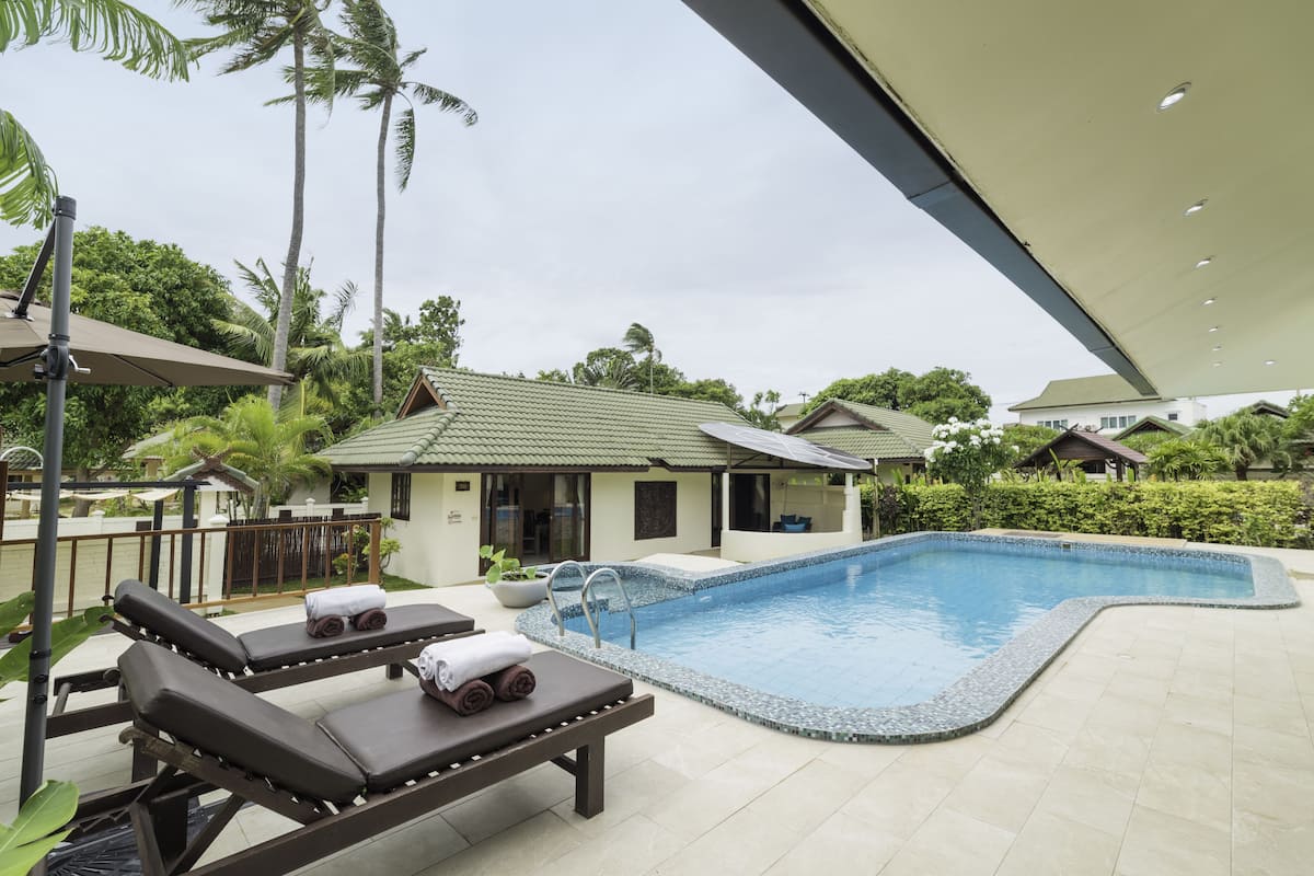 A swimming pool area with lounge chairs, a covered seating area, and a building with a green roof.