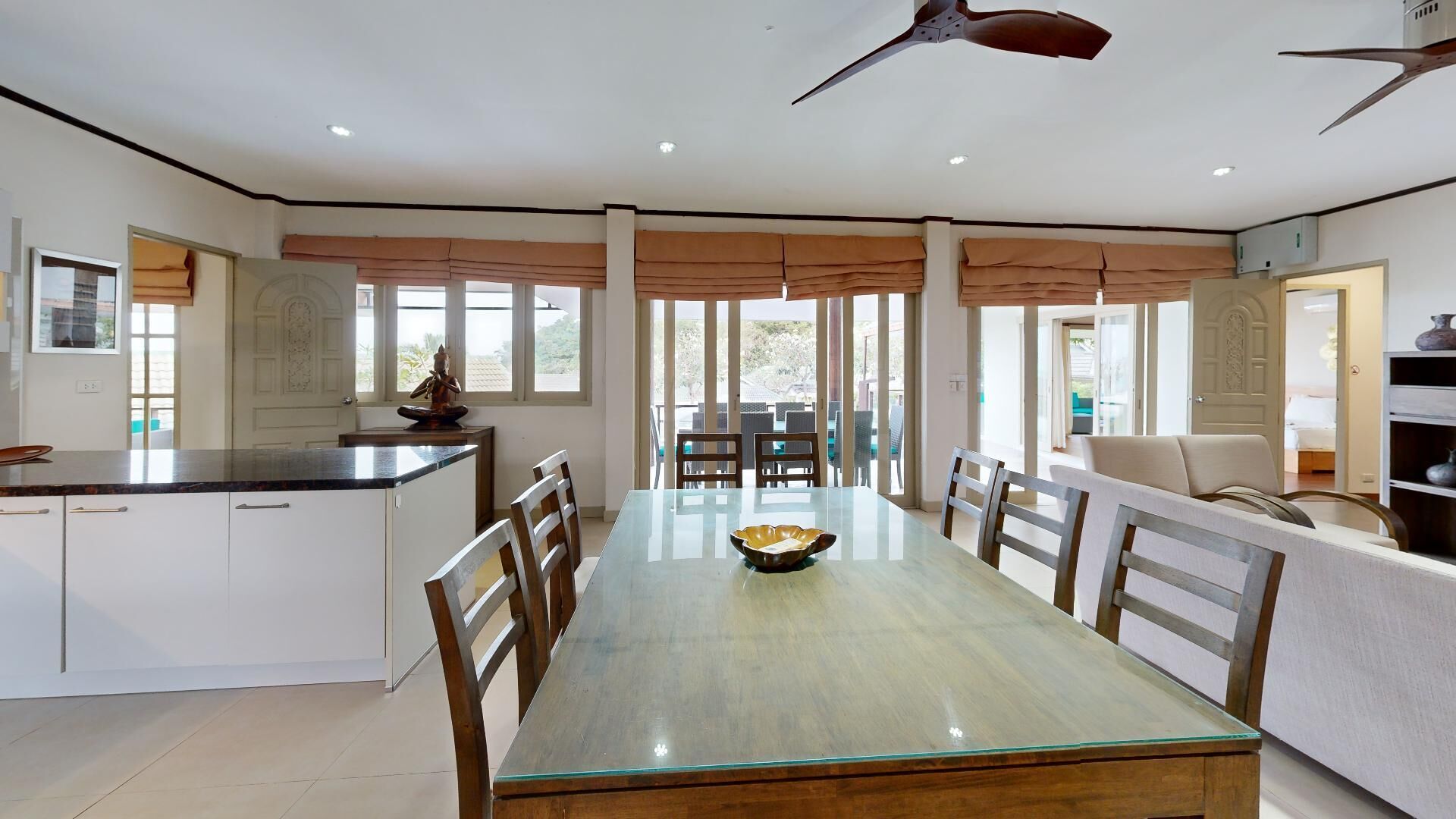 A spacious dining area with a glass-top table, wooden chairs, and a ceiling fan.