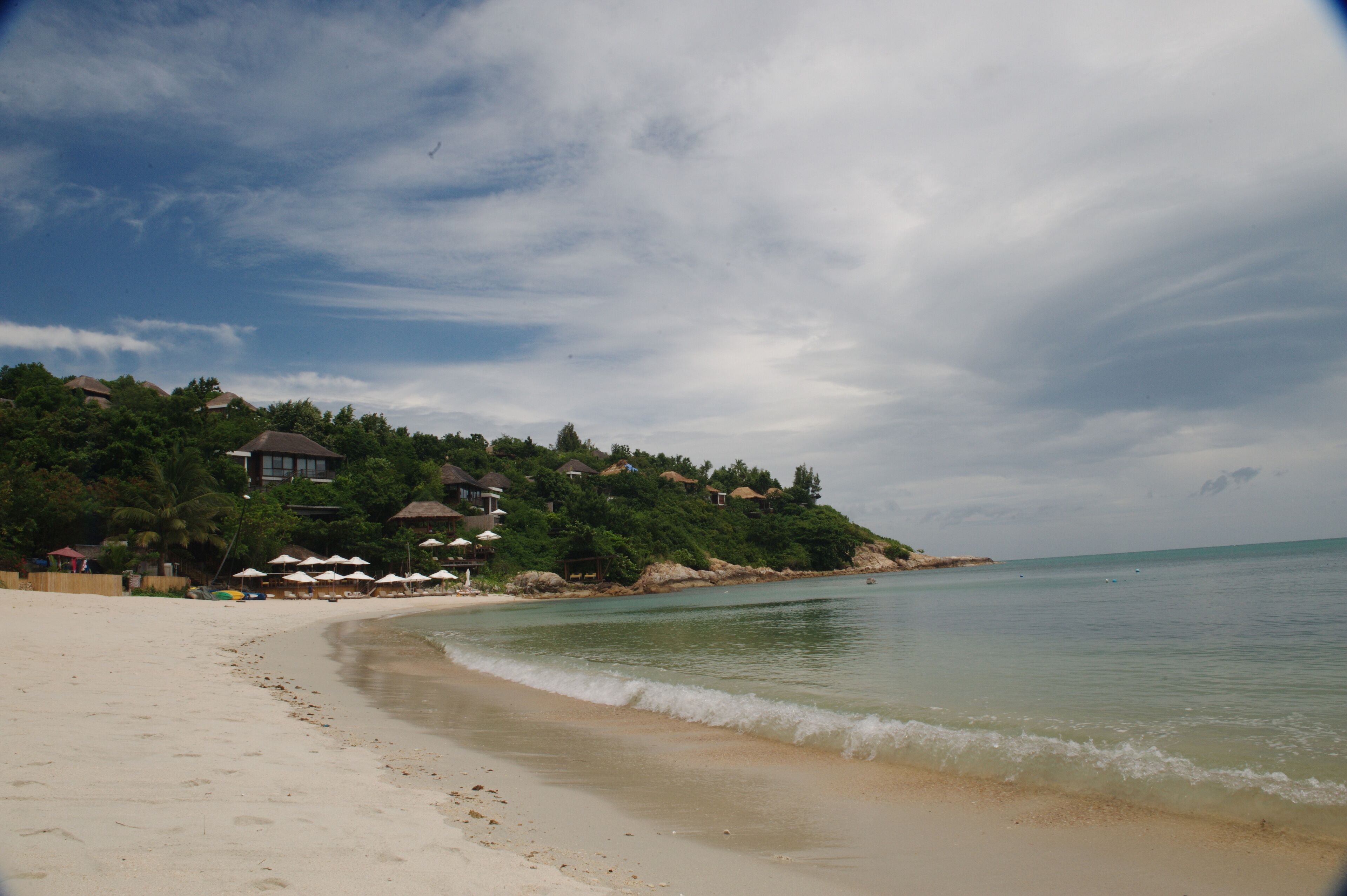 Uma praia com uma fileira de guarda-sóis e uma fileira de casas com telhados de palha.