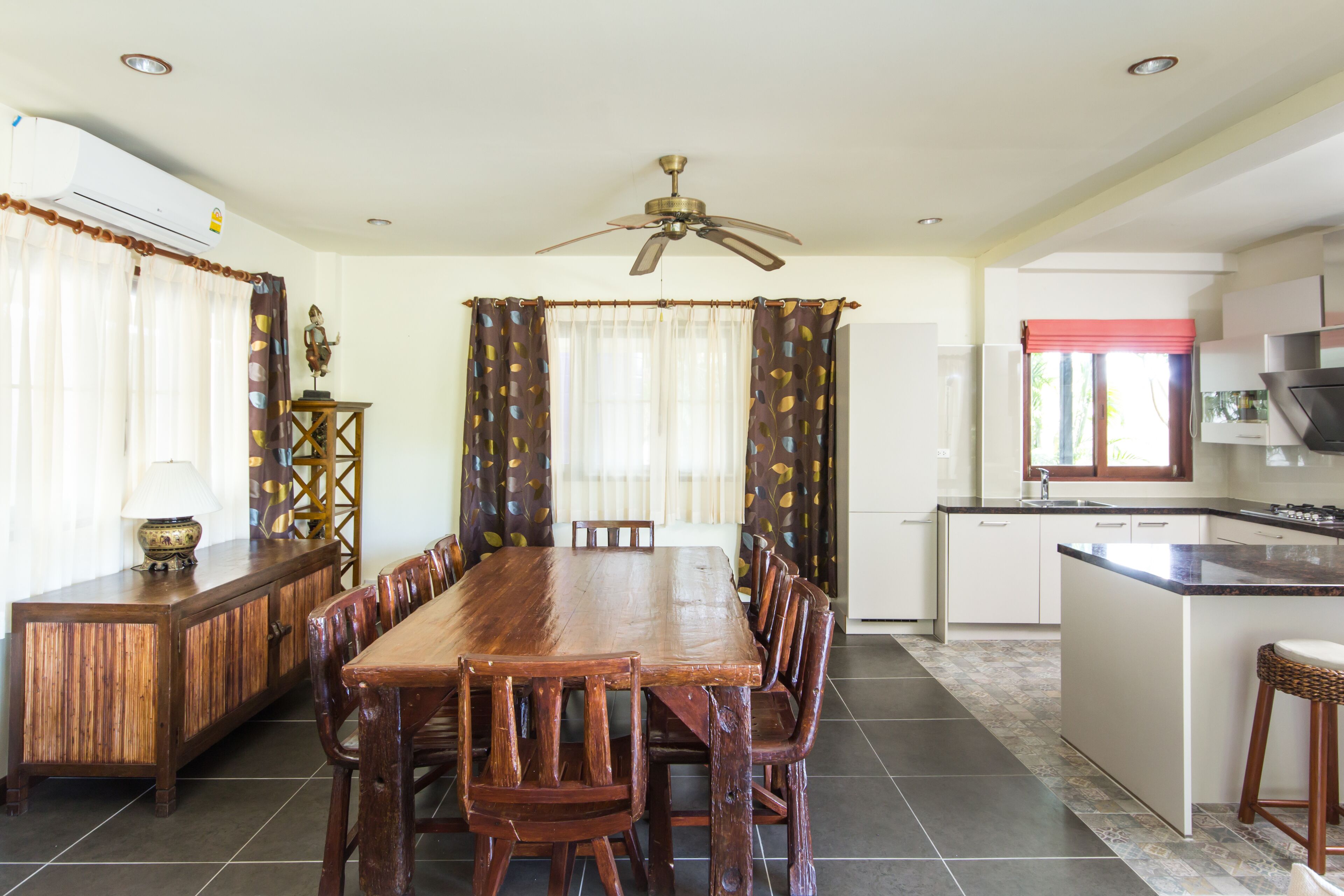 A spacious dining area with a wooden table and chairs, a ceiling fan, and a kitchen area with a refrigerator and sink.