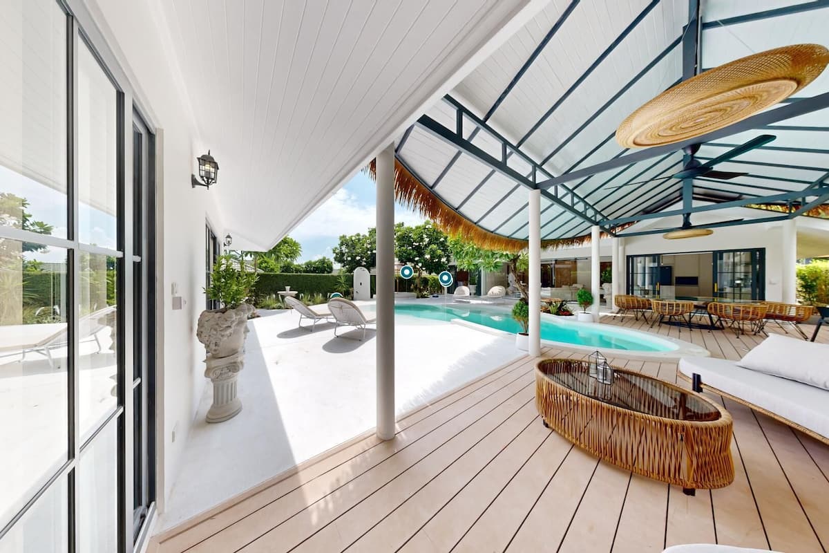 A modern outdoor pool area with lounge chairs, a wicker sofa, and a glass ceiling.