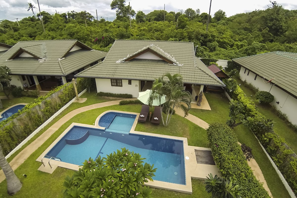 A residential complex with multiple houses, a swimming pool, and well-maintained gardens.