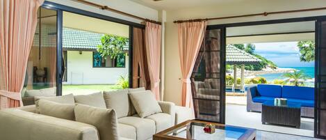 A spacious living area with a beige sofa, a glass coffee table, and a view of a blue outdoor seating area and a beach.