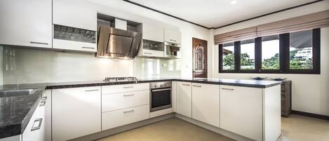 A modern kitchen with white cabinets, a stainless steel range hood, and a large window with a view of greenery.
