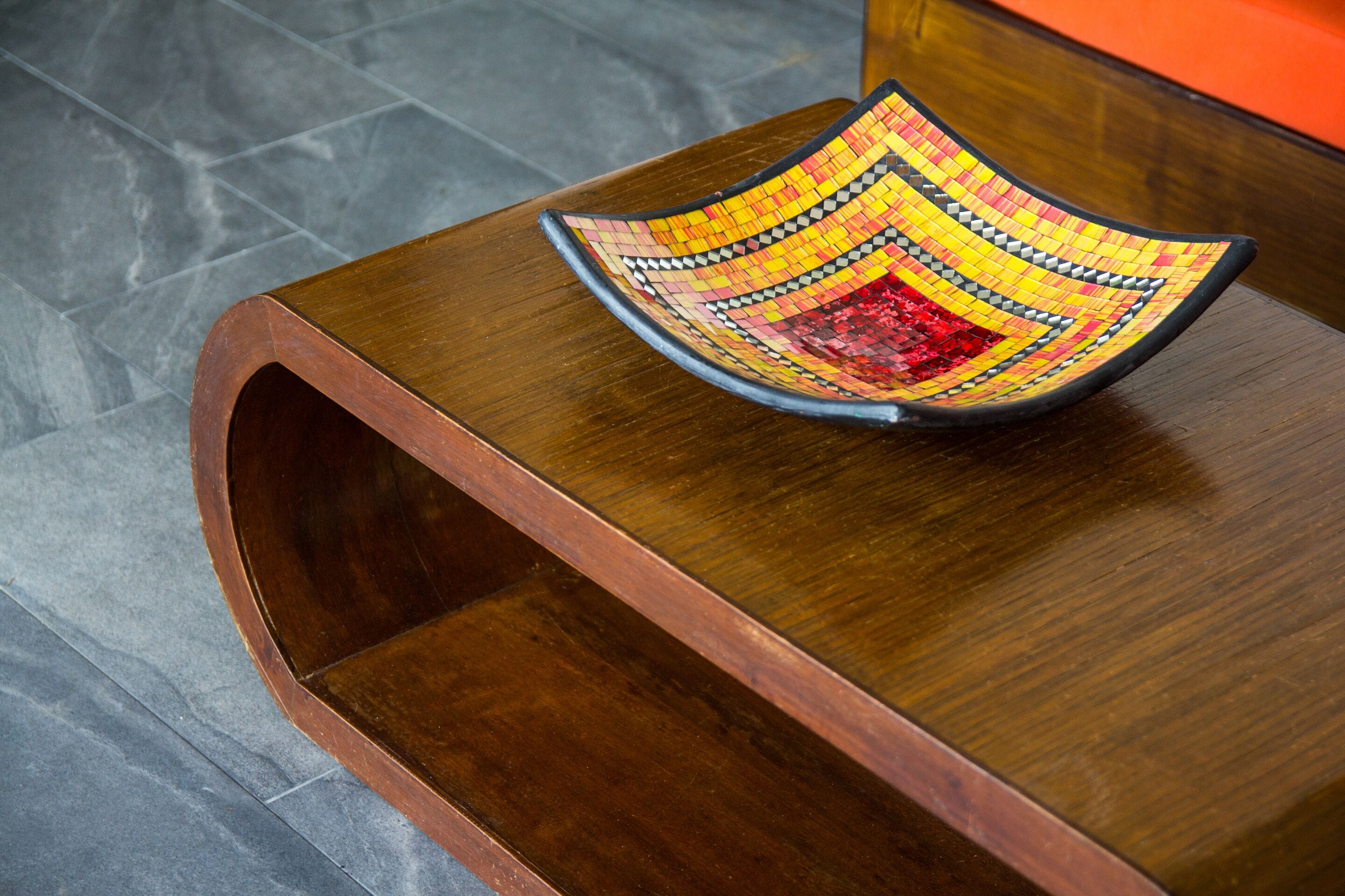 A wooden table with a colorful mosaic bowl on top.