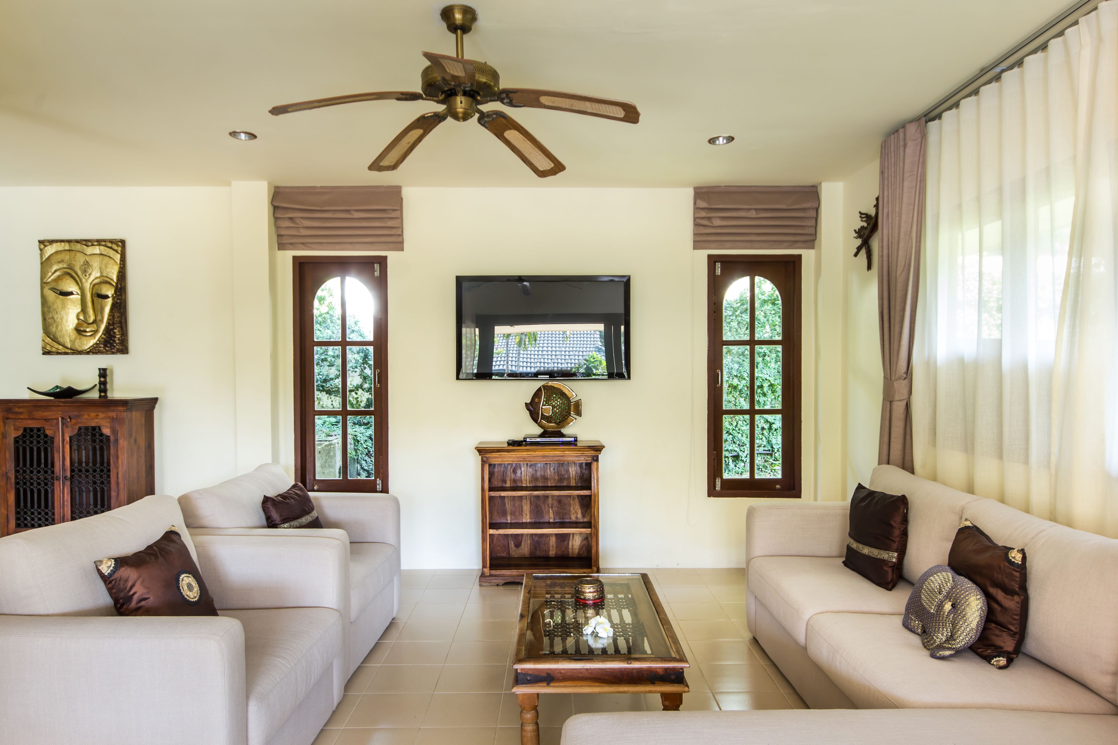 A living room with a sofa set, a coffee table, a ceiling fan, a television, and a window with curtains.