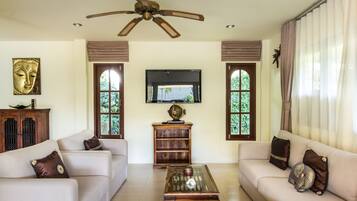 A living room with a sofa set, a coffee table, a ceiling fan, a television, and a window with curtains.