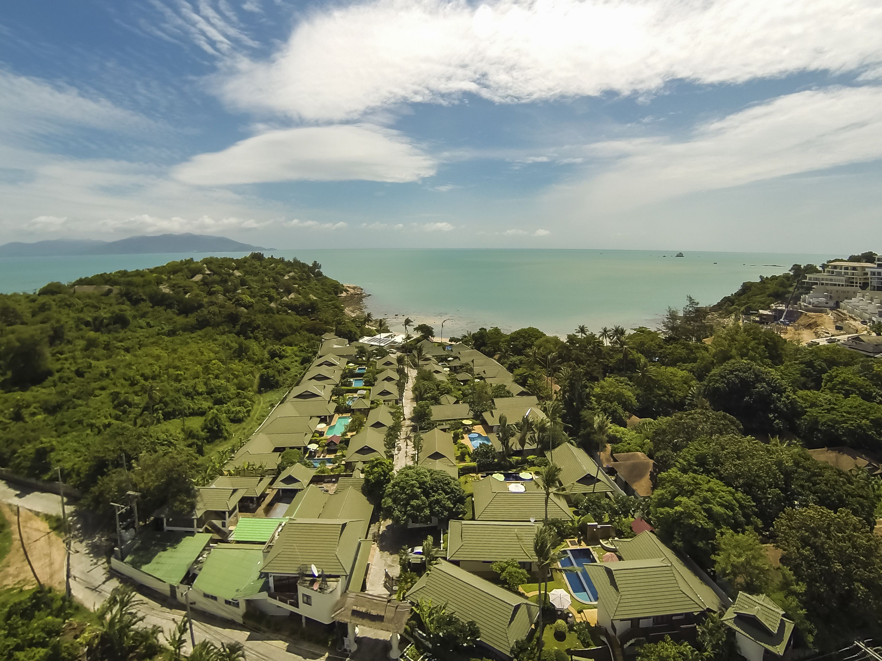 A resort with multiple bungalow-style buildings, a central pathway, and a view of the beach and sea.