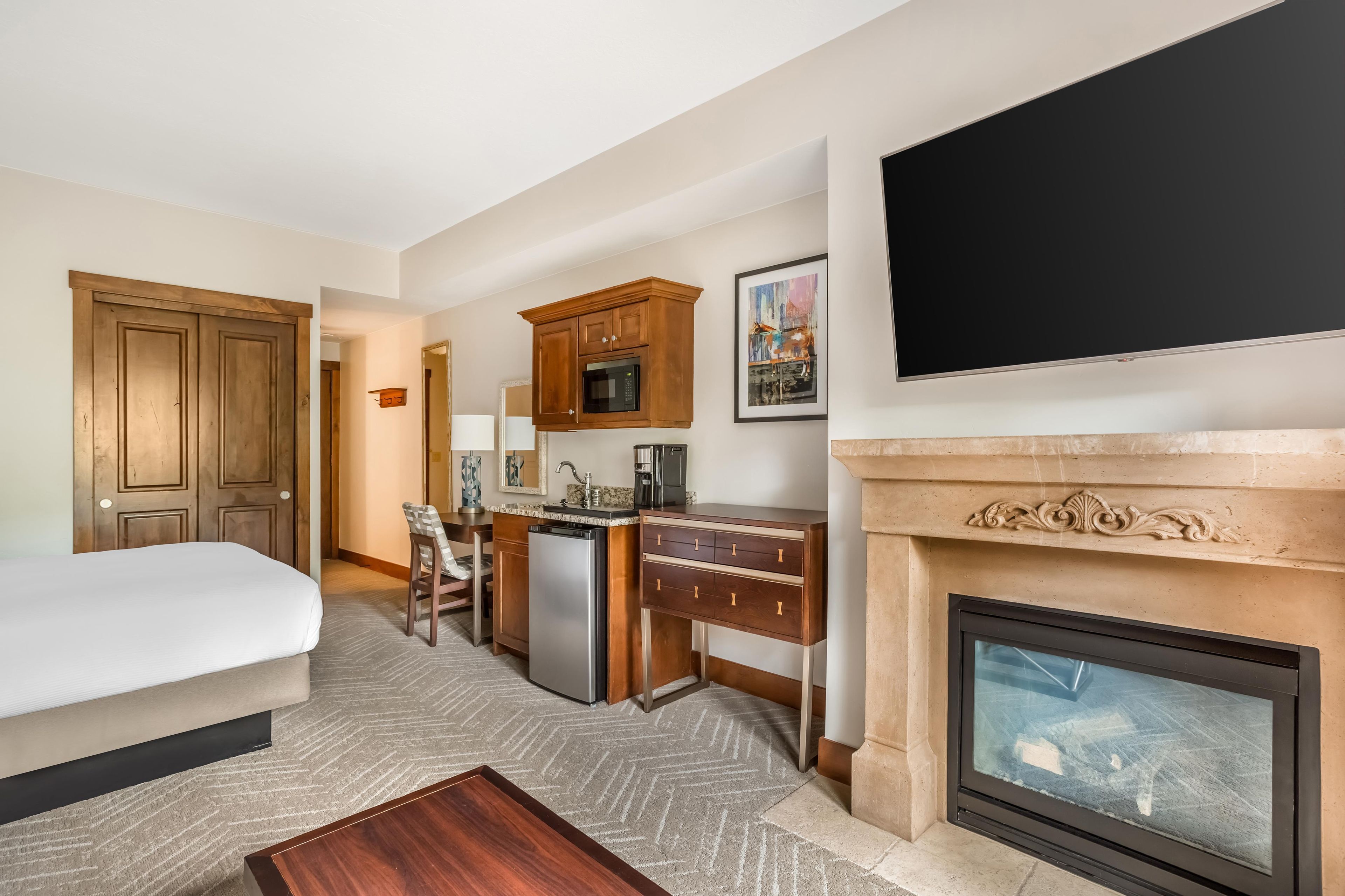 Una habitación de hotel con una cama, un escritorio, una kitchenette, una chimenea y un televisor.