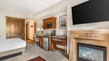 A hotel room with a bed, a desk, a kitchenette, a fireplace, and a television.