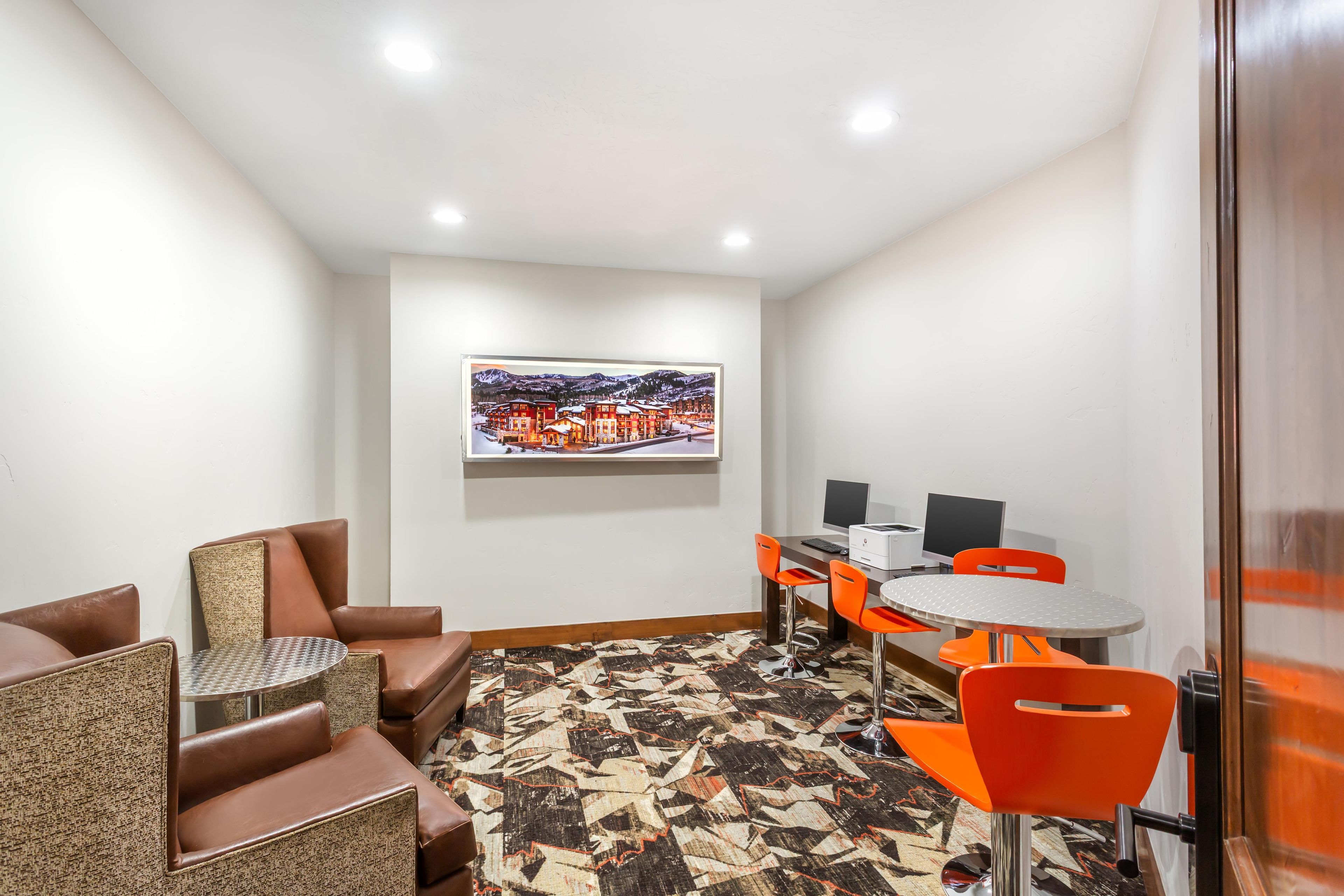 A hotel room with a seating area, a desk with a computer, and a framed picture on the wall.