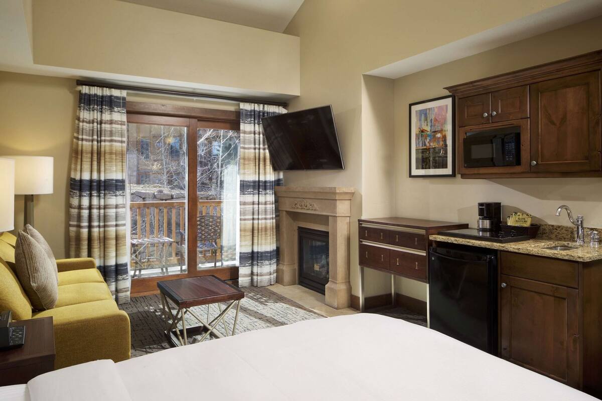 A hotel room with a bed, a desk, a fireplace, a television, and a kitchen area.