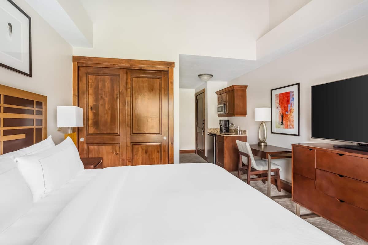 A hotel room with a large bed, wooden wardrobe, desk, chair, and a flat-screen TV.