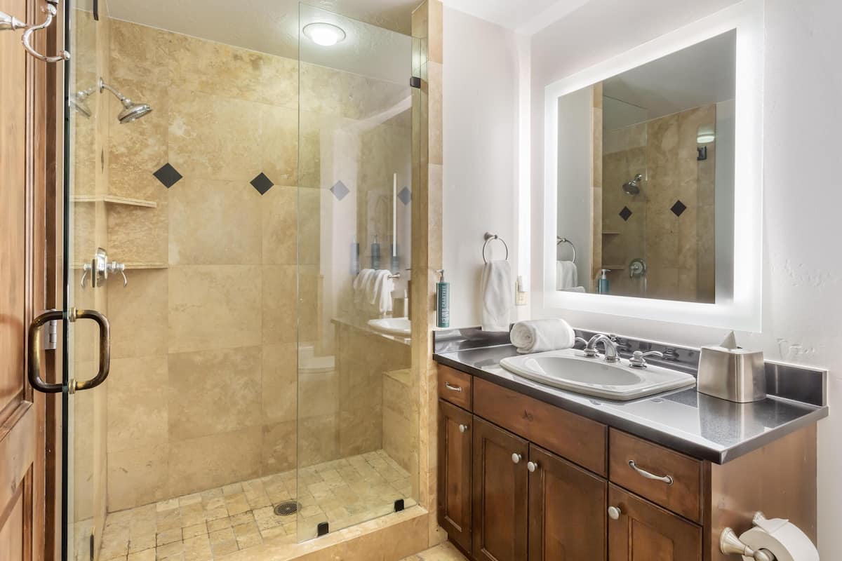 A modern bathroom with a glass-enclosed shower, a large mirror, and a wooden vanity with a sink.