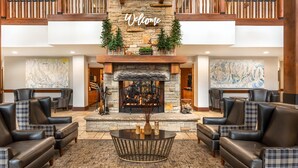 A lobby with a stone fireplace, leather sofas, a 'Welcome' sign, and a view of the city. - Hilton Grand Vacations Club Sunrise Lodge Park City (Park City)