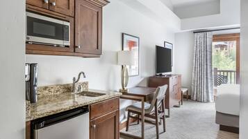 A hotel room with a kitchenette, a bed, a TV, and a window with curtains.