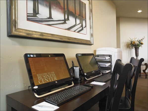 A business center with two HP laptops, a keyboard, a mouse, and a printer on a desk.