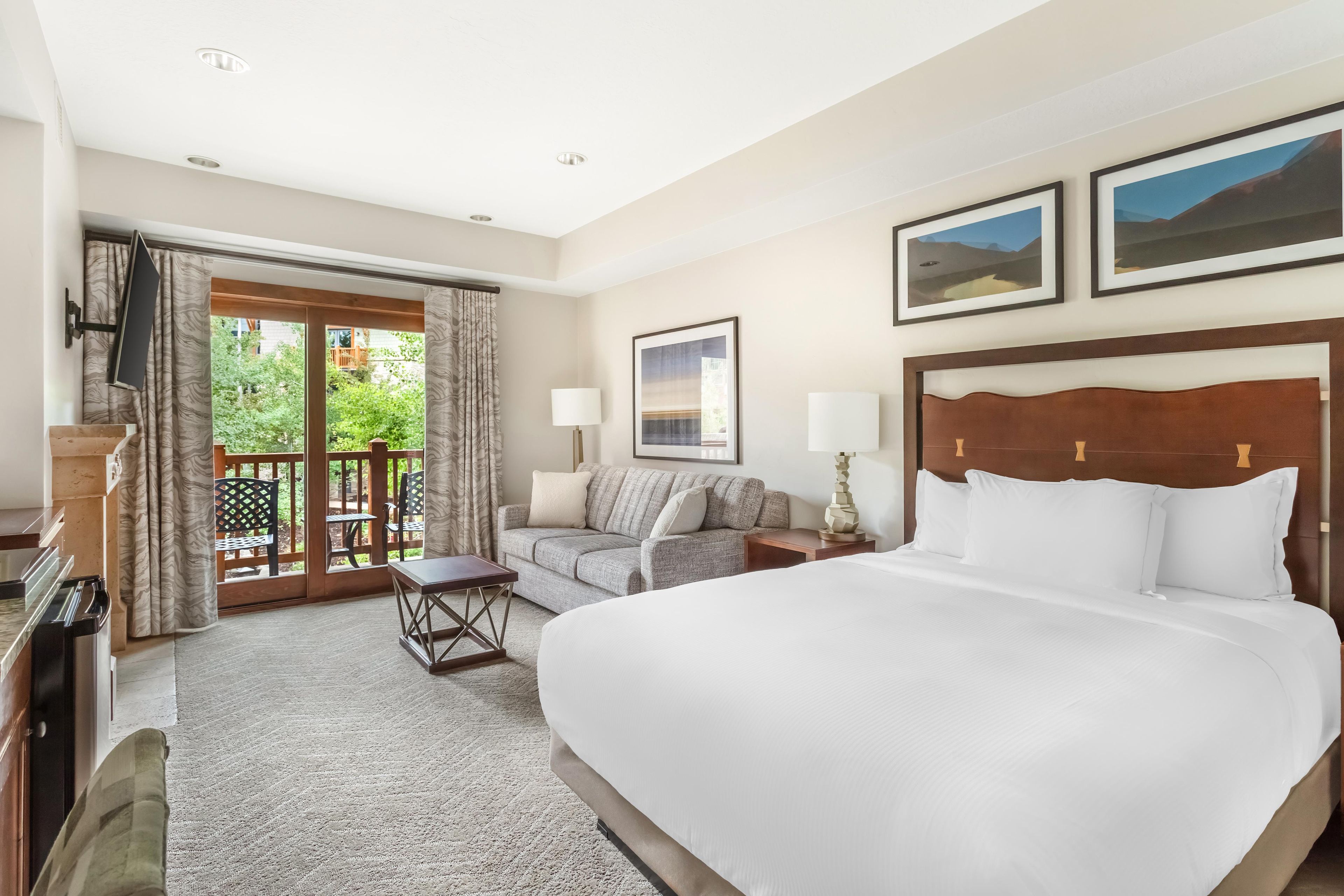 A hotel room with a large bed, a sofa, a desk, and a balcony with curtains.