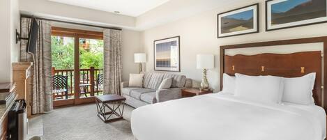 A hotel room with a large bed, a sofa, a desk, and a balcony with curtains.