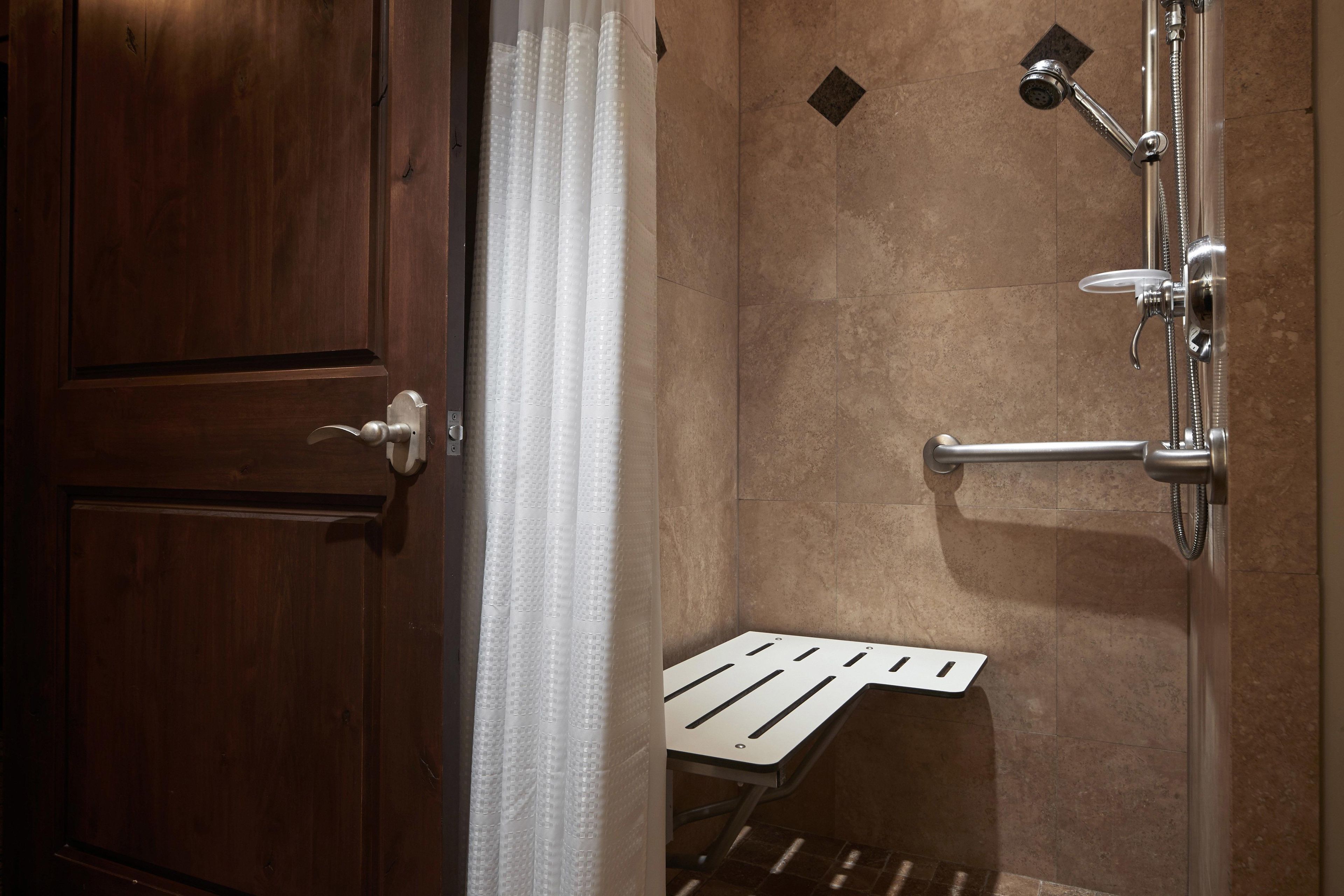 Une douche équipée d’un pommeau de douche à main et d’un robinet mural, ainsi que d’un porte-serviettes et d’une petite étagère.