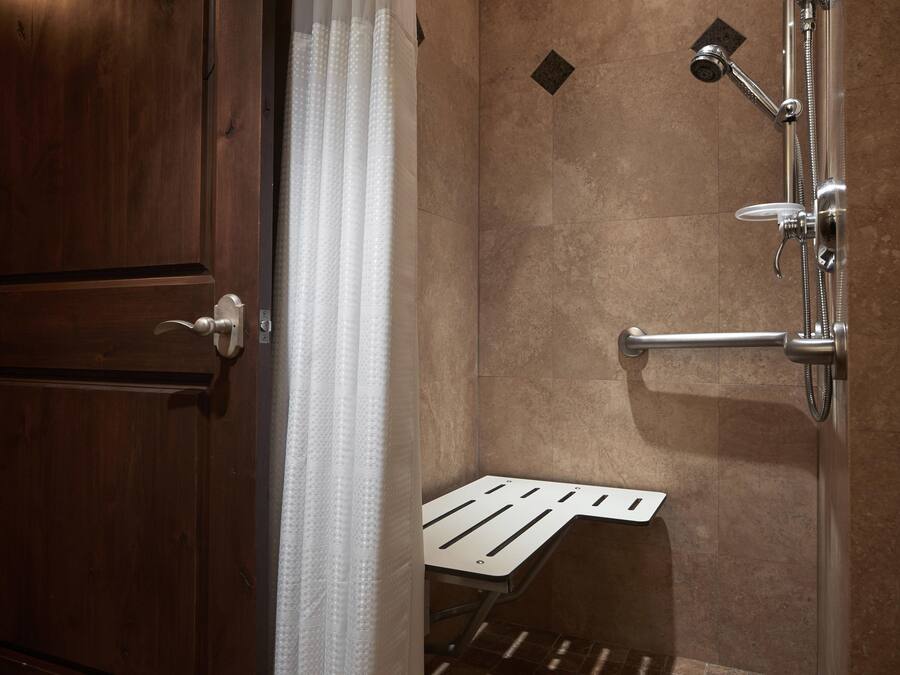 A shower with a handheld showerhead and a wall-mounted faucet, a towel rack, and a small shelf.
