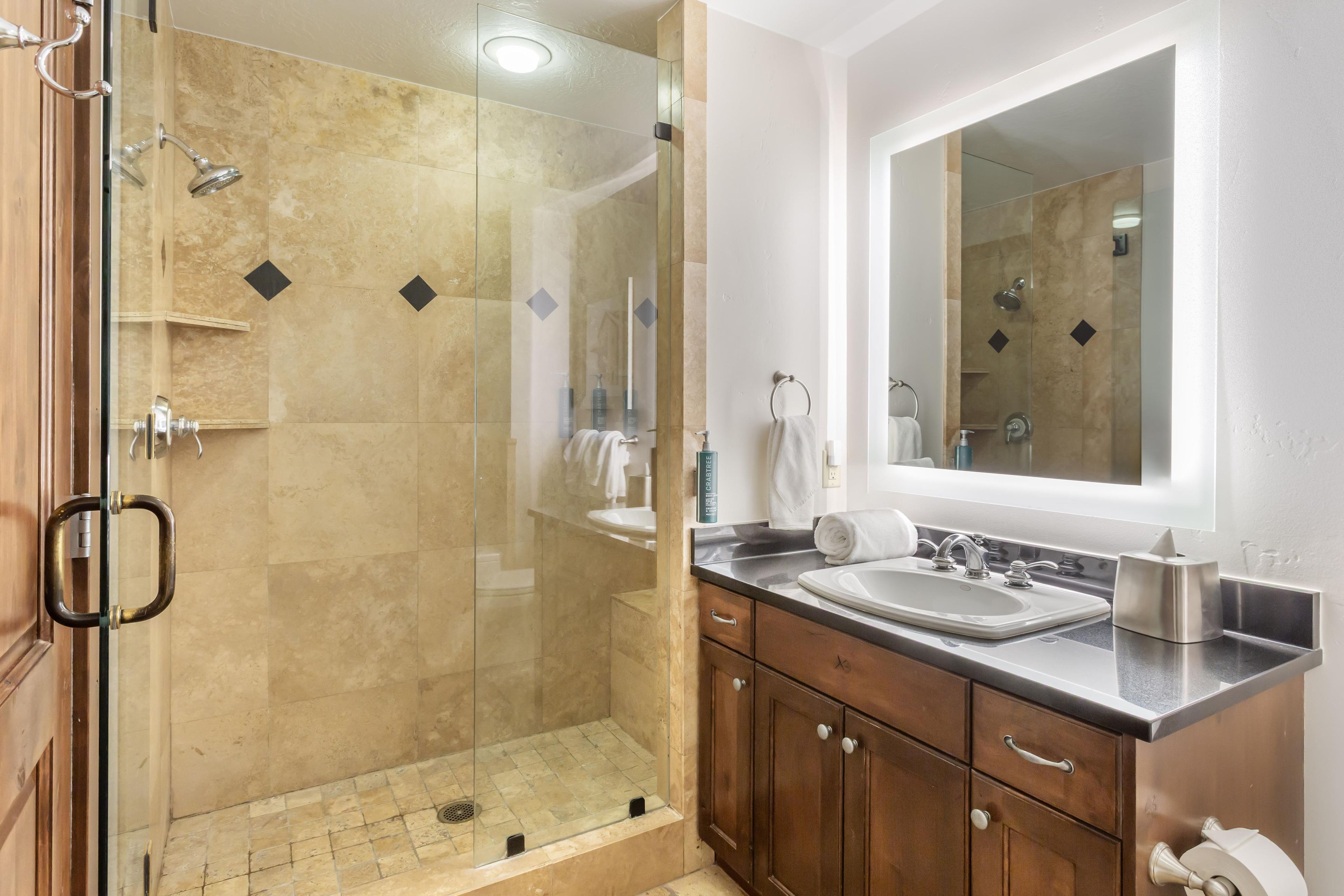 A modern bathroom with a glass-enclosed shower, a sink with a mirror above, and wooden cabinets.