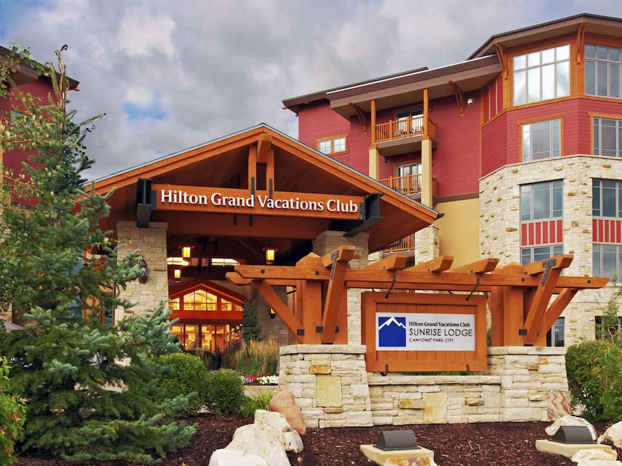 Un hôtel doté d’une entrée imposante, d’une façade en pierre et d’une enseigne indiquant qu’il fait partie du réseau Hilton Grand Vacations Club.
